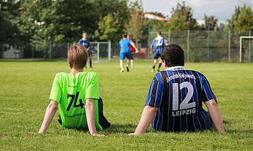 Zwei Fußballspieler sitzen auf dem Rasen und sind von hinten zu sehen