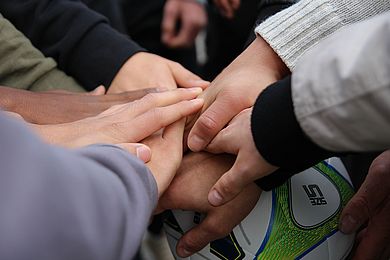 Mitglieder der Fußballmannschaft haben die Hände vorm Spiel aufeinandergelegt.