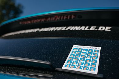 Rückseite eines Autos von Porsche mit dem Fingeralphabet der Deutschen Gebärdensprache auf einer Karte