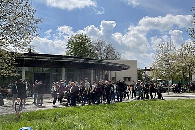 Vor dem Freizeithaus des Berufsbildungswerkes stehen viele Menschen in Gruppen zusammen.