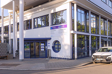 Haupteingang der Witzgallstraße 6 mit der Beschilderung für das BBW und die Diakonie am Thonberg. Der Eingang befindet sich unter einem Vordach, das von hohen Säulen getragen wird. Rechts am Haus ist eine große Fensterfront. Ein helles Auto parkt davor.