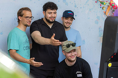 4 Männer vor einer blauen Wand. Sie schauen alle in eine Kamera.
