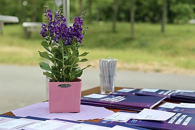 Auf einem Tisch liegen Flyer und Broschüren der BBW-Leipzig-Gruppe in Lila. Die Farbe ist das Erkennungsmerkmal des Unternehmensverbundes und ziert auch ein Blümchen, das als Dekoration mit dazu gestellt wurde.