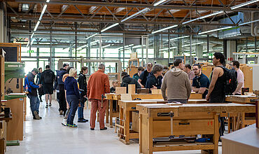 Viele Personen im Fachbereich Holztechnik. Die Gäste stehen verteilt zwischen Werkbänken und Arbeitstischen. 