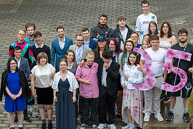Gruppenfoto der Absolvent*innen. Auf der rechten Seite halten 3 Personen eine große pinke "35" in den Händen