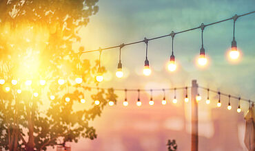 Lichterkette im Garten mit blau-rosa Farbverlauf des Himmels