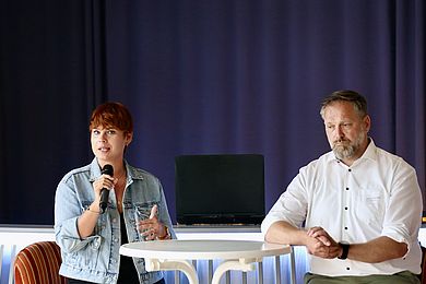 Thomas Rusch (Teamleiter Arbeitgeberservice von der Agentur für Arbeit) und Ira Kummrow (Abteilungsleiterin des Kompetenzzentrum für Vermittlung und Integration der BBW-Leipzig-Gruppe) bei der Podiumsdiskussion. Er trägt ein weißes Hemd und einen grau melierten Bart. Frau Kummrow hat kurze, rot gefärbte Haare und trägt eine Jeansjacke. 