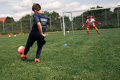 Teilnehmer der Fußballschule schießt auf das Tor - Bulli als Torwart