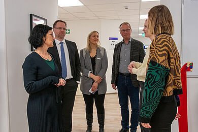 Mehrere Personen hören zwei jungen Frauen zu, die etwas erklären