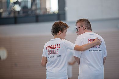 Zwei Teilnehmende der RB Fußballschule in der Sporthalle. Ein Junge hat den Arm um einen anderen Jungen gelegt.