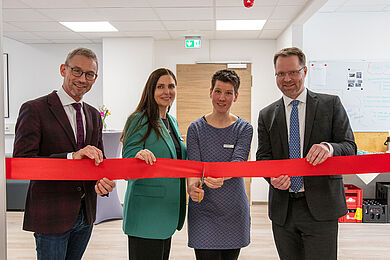 Vier Personen halten ein rotes Satin-Band. Von links: Prof. Dr. med. Fuchs, Claudia Rodegast, Lea Beuter, die die Schere angesetzt hat, und Bastian Schmiedel