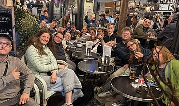 Eine Gruppe von Menschen sitzt und steht in einem belebten Café.